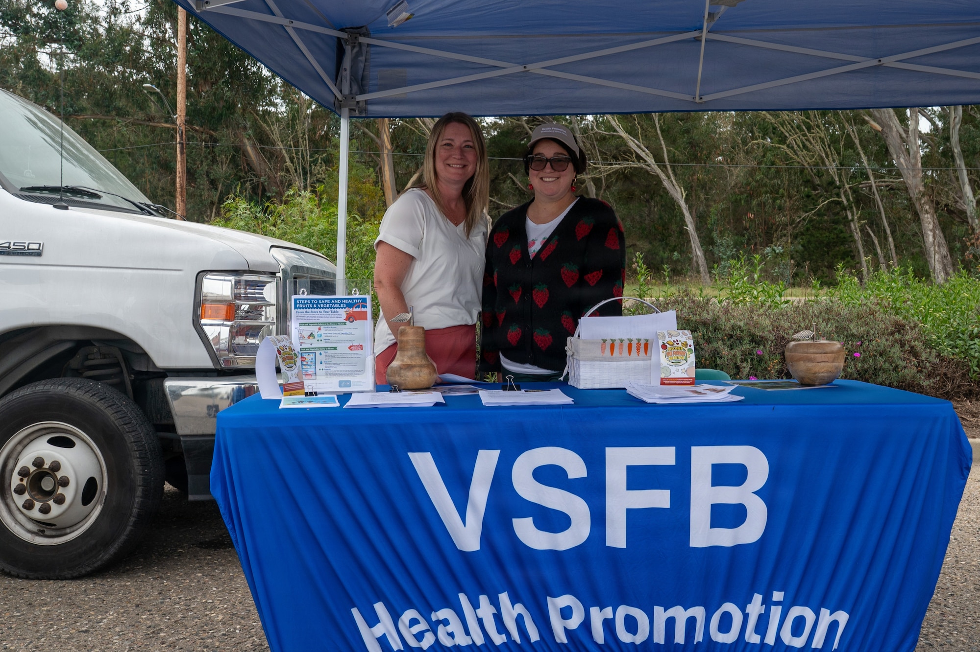 Two people stand side by side for a photo behind a table booth.