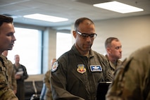 Gen. Spain looks down on a computer with other Airmen in the background stand around the room.