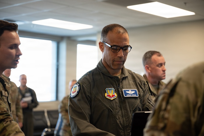 Gen. Spain looks down on a computer with other Airmen in the background stand around the room.