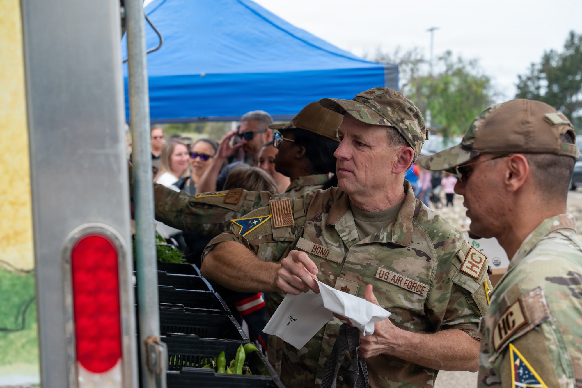 A person holds a back in their hand while in line at a farmer's market truck event.
