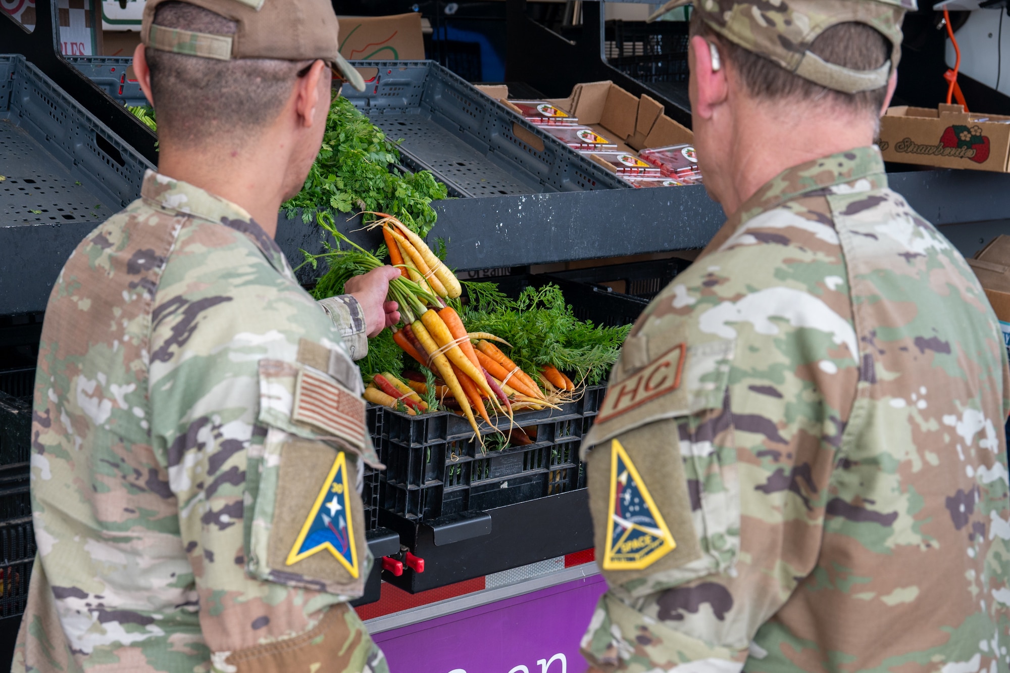 Two people reach out for produce from the side of a farmer's market truck.