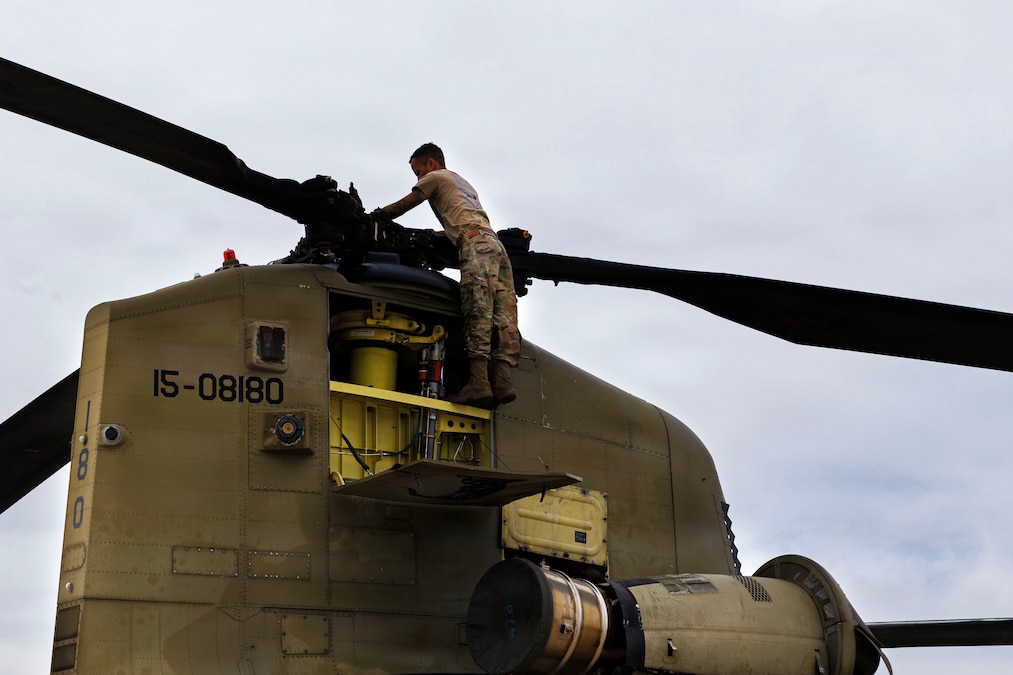 A soldier works high up on a rotor on the top of an aircraft.