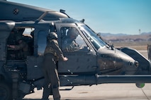 An Airman assists Gen. Adrian Spain as he gets situated in an HH-60W Jolly Green II helicopter on the helicopter pad at Nellis Air Force Base.