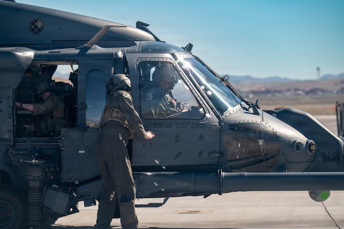 An Airman assists Gen. Adrian Spain as he gets situated in an HH-60W Jolly Green II helicopter on the helicopter pad at Nellis Air Force Base.