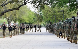 A group of military members carry back backs while marching in formation.