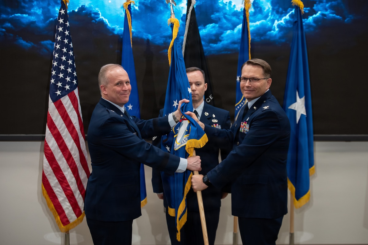 Brig. Gen. Jason Bartolomei, left, commander of the Air Force Research Laboratory, passes command of AFRL’s 711th Human Performance Wing to Col. Dale Harrell, right, while Master Sgt. Justin Knowles, first sergeant for the Wing, stands center during a change of command ceremony at Wright-Patterson Air Force Base, Ohio, March 30, 2026.