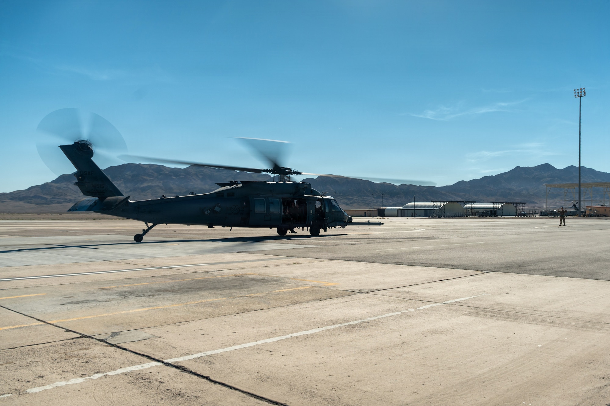 An HH-60W Jolly Green II helicopter taxis on the helipad.