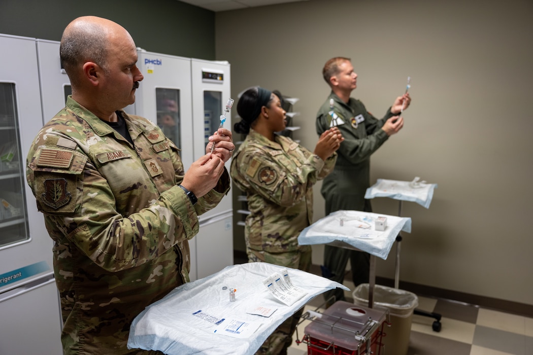 U.S. Air Force Col. Richard Kind, 97th Air Mobility Wing (AMW) commander, right, and Chief Master Sgt. Jonny Adams, 97th AMW command chief, left, are taught syringe techniques by Tech. Sgt. Logan McEachin, Altus Medical Group Healthcare Readiness Squadron primary care flight chief, center, at Altus Air Force Base, Oklahoma, April 24, 2026. The demonstration included proper injection techniques using medical training mannequins. (U.S. Air Force photo by Airman 1st Class Nathan Langston)