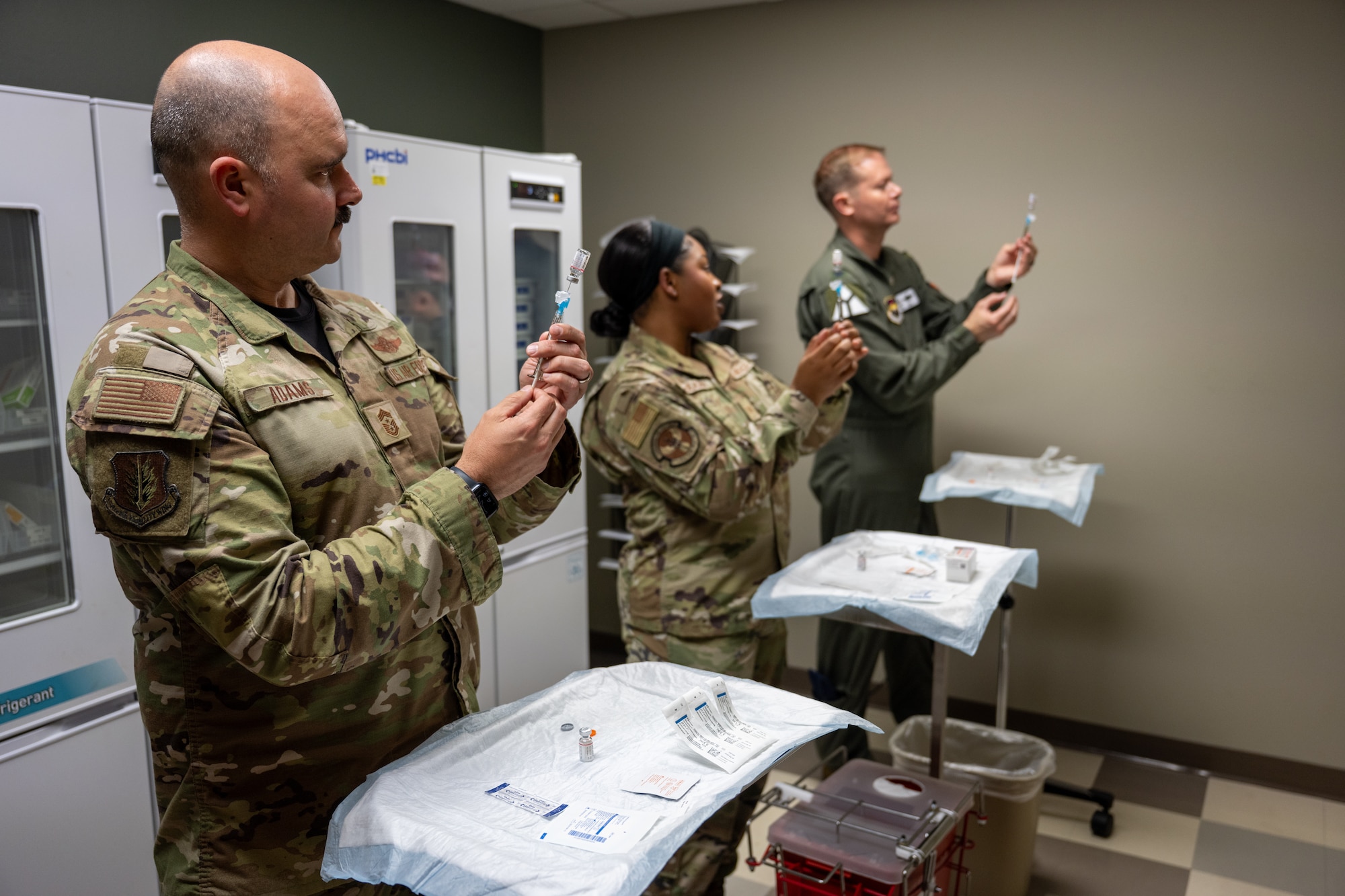 U.S. Air Force Col. Richard Kind, 97th Air Mobility Wing (AMW) commander, right, and Chief Master Sgt. Jonny Adams, 97th AMW command chief, left, are taught syringe techniques by Tech. Sgt. Logan McEachin, Altus Medical Group Healthcare Readiness Squadron primary care flight chief, center, at Altus Air Force Base, Oklahoma, April 24, 2026. The demonstration included proper injection techniques using medical training mannequins. (U.S. Air Force photo by Airman 1st Class Nathan Langston)