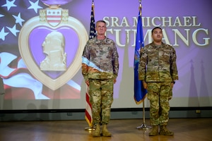 Two men in camouflage stand at attention on a stage.