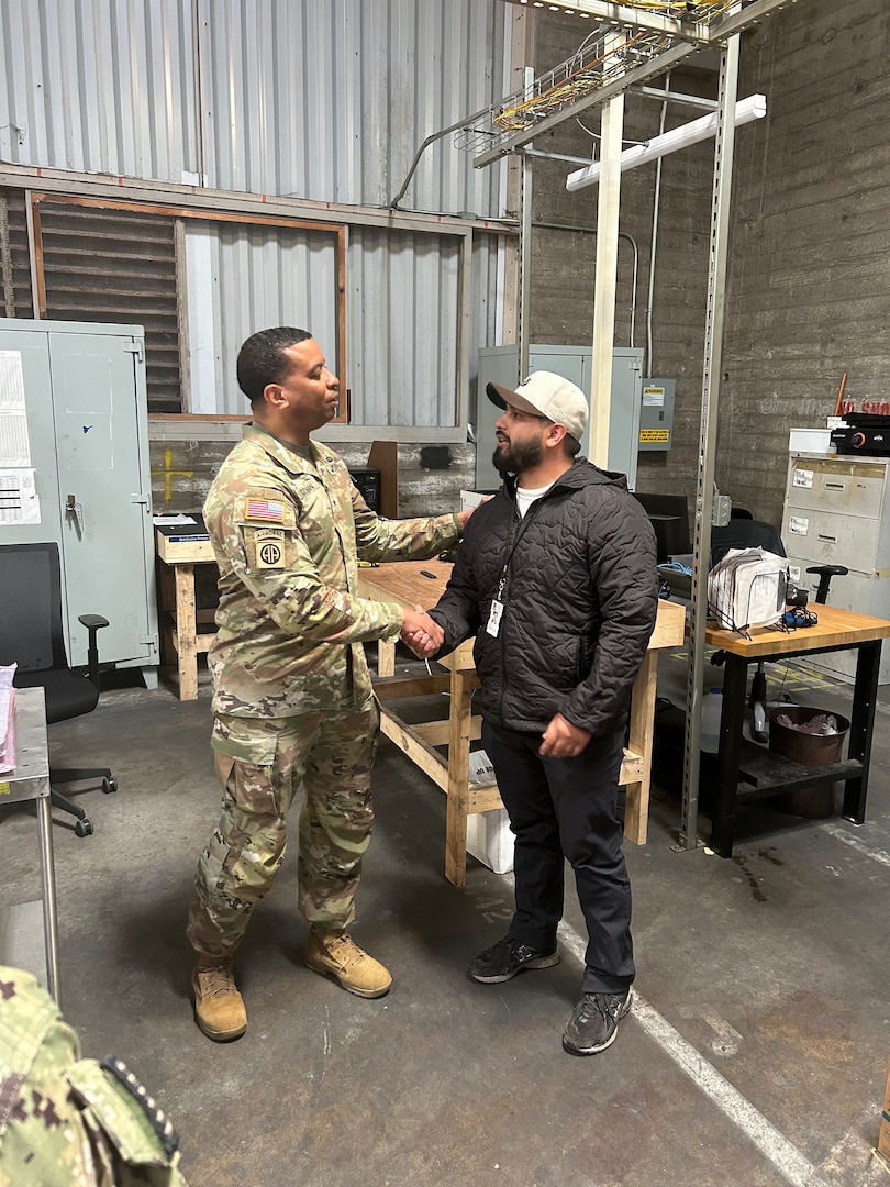 A military member shaking hands with a civilian employee in a warehouse environment.