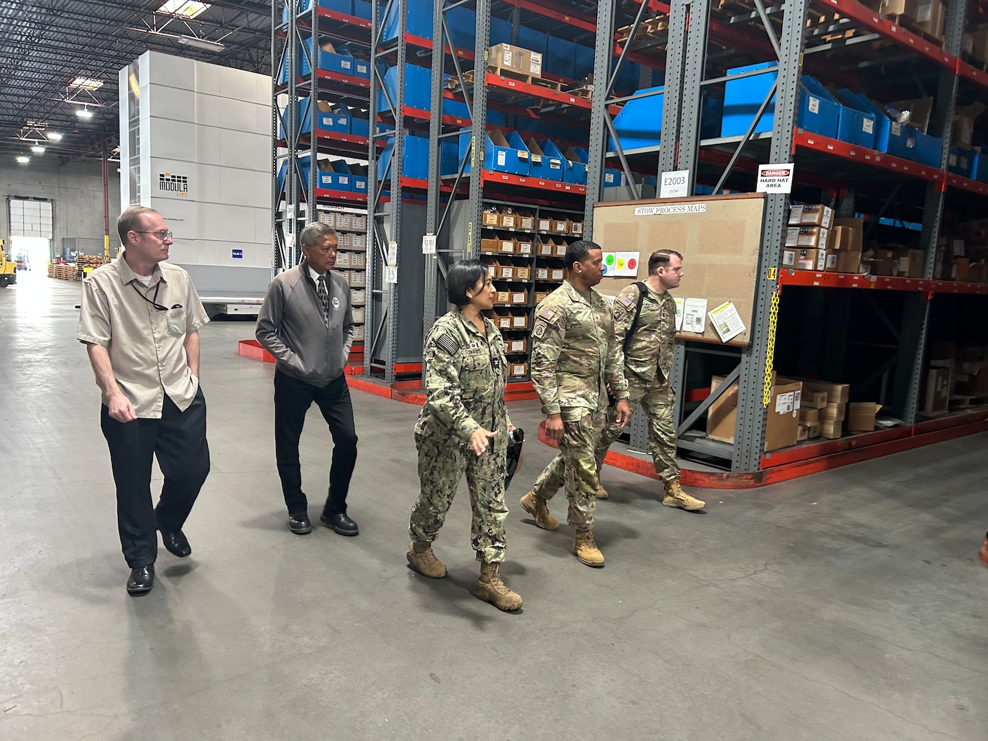Military and civilians walking through a warehouse.
