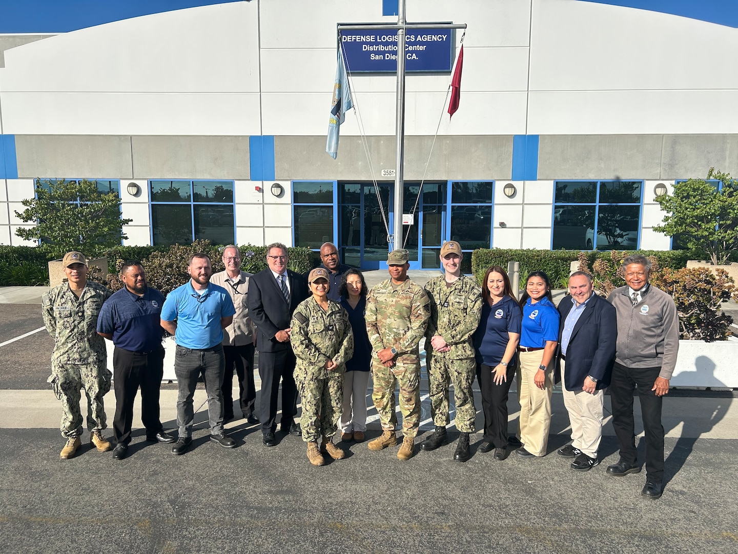 A group photo of military and civilians in front of a building.