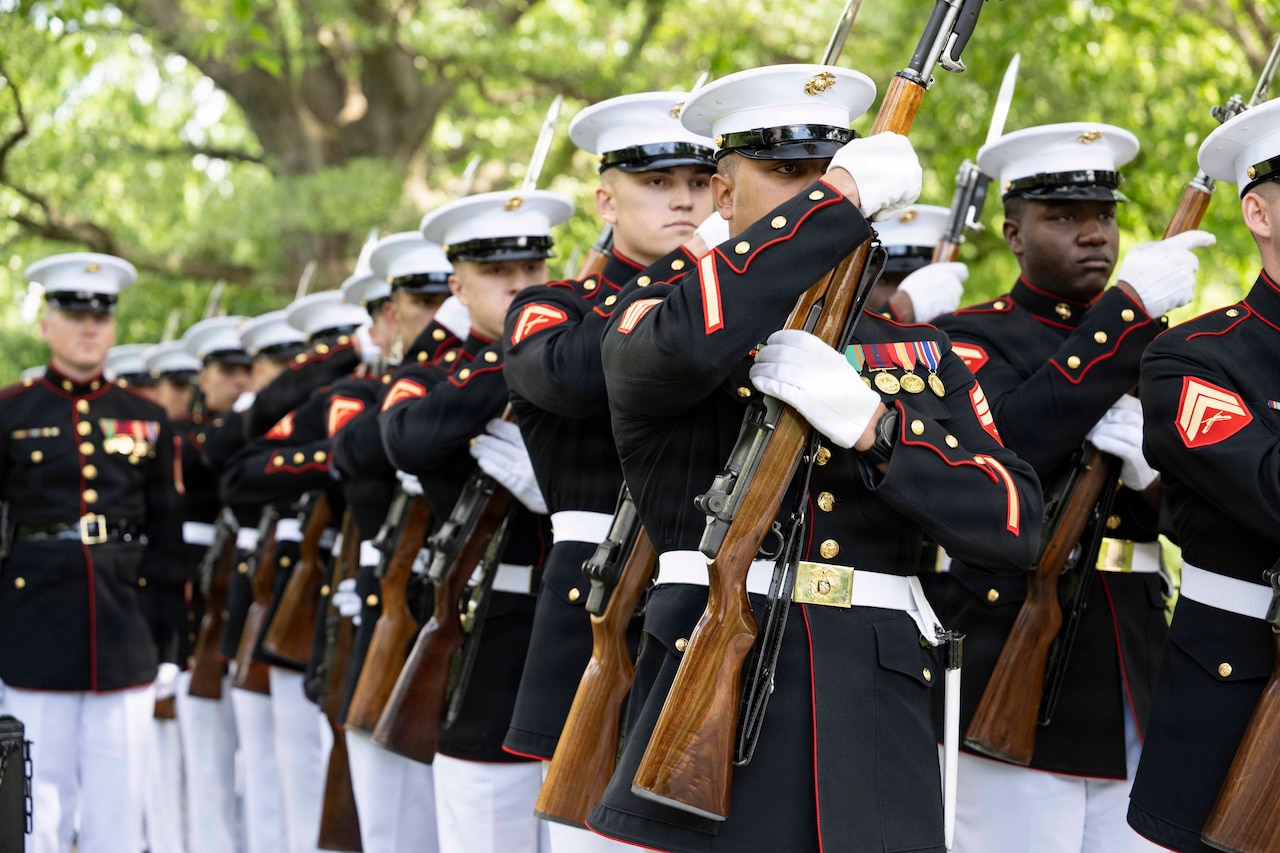 A group of people wearing military dress uniforms hold rifles while standing in formation.