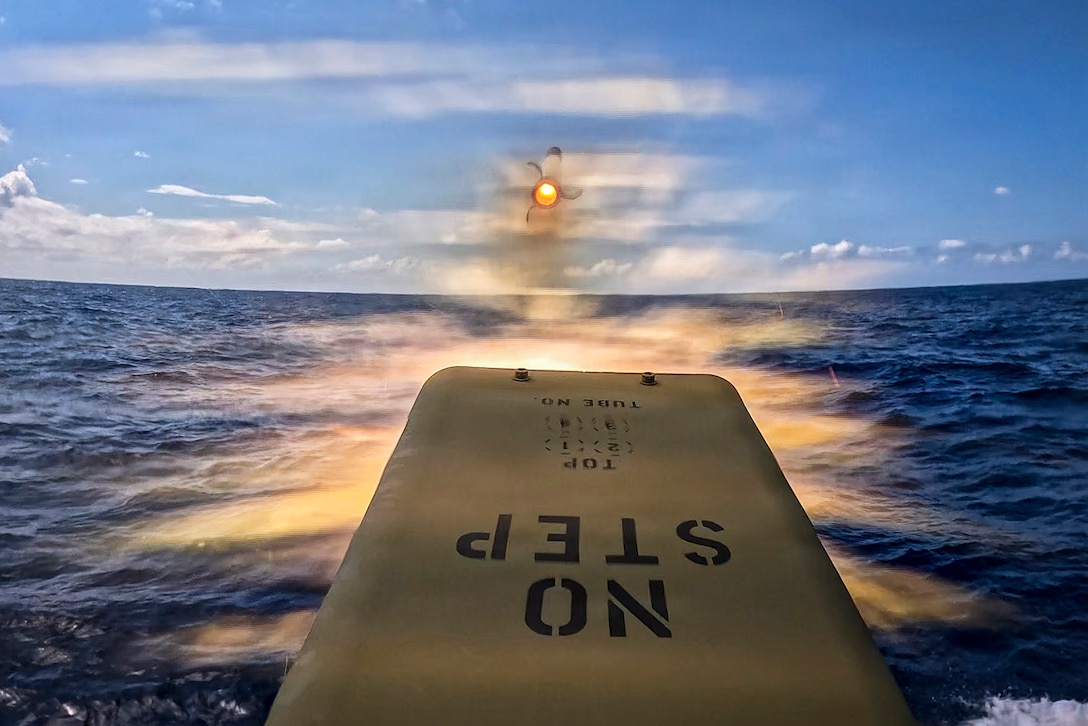An unmanned surface vehicle launches a rocket leaving an orange glow on blue waters during the day.