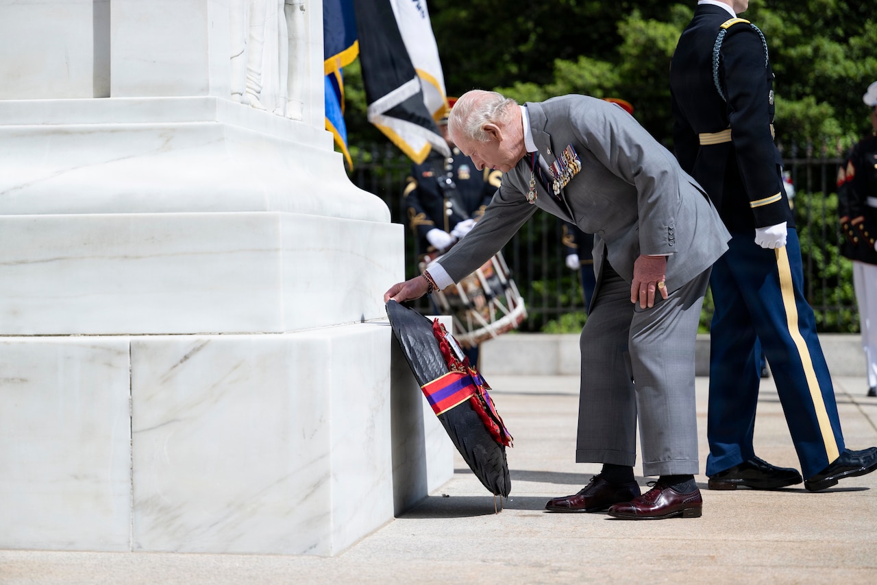 A man wearing a suit bends over to lay a wreath at the base of a marble memorial.
