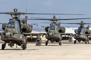 Three military helicopters sit near each other on a cement airfield.