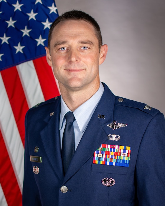 Service member poses for official portrait in front of US flag wearing their service dress blues
