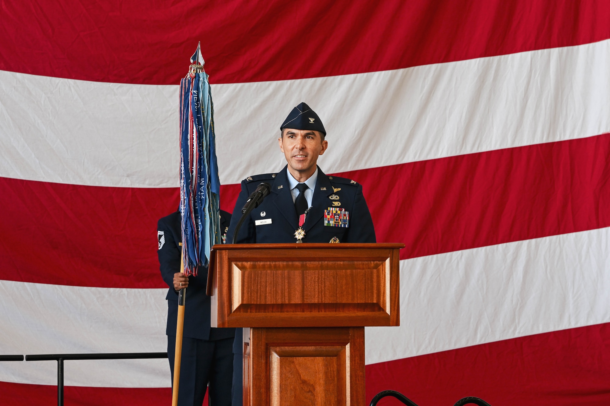 An Airman stands behind a podium on stage giving a speech.