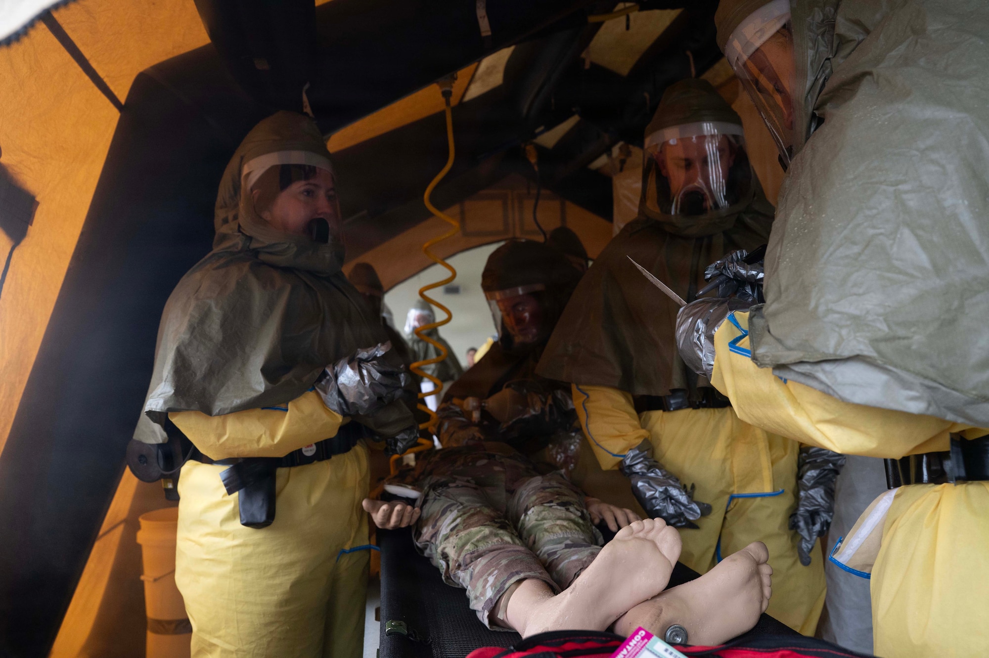 People stand around a mannequin while in personal protective suits in a tent.