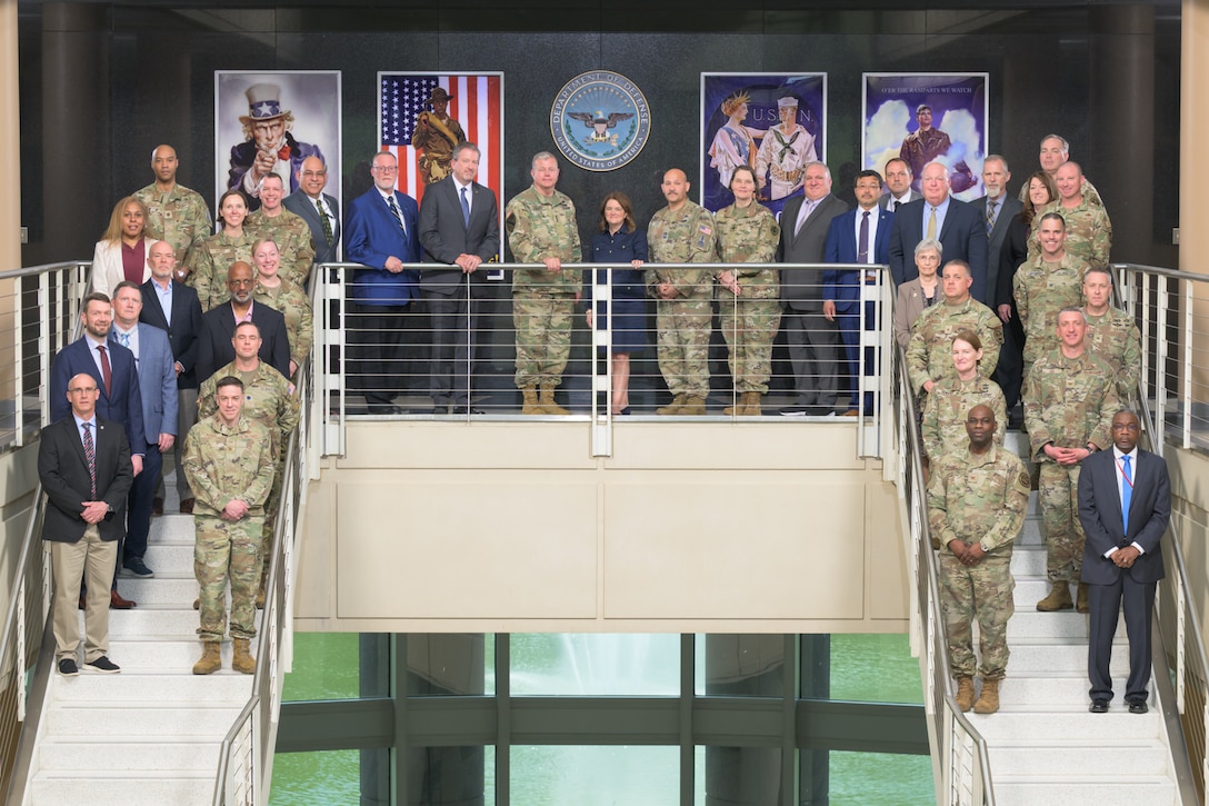 A group of people, some in civilian business clothes and some in military uniforms, pose on a staircase.