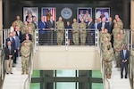 A group of people, some in civilian business clothes and some in military uniforms, pose on a staircase.