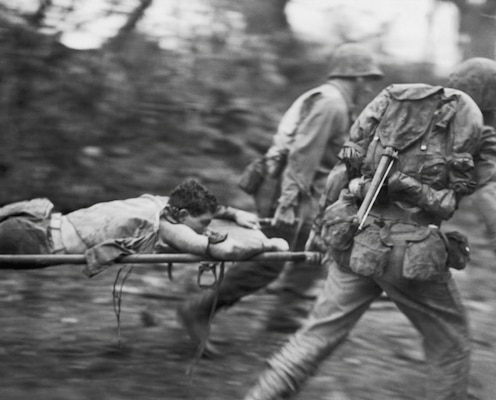 U.S. service members carry a wounded Marine on a stretcher to a medical aid station during the Battle of Okinawa in 1945. Corpsmen and medical personnel worked under constant enemy fire to evacuate and treat casualties throughout the campaign. (U.S. Marine Corps photo)