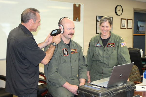 U.S. Navy Lieutenant Commander Juliette Ruff, a Naval Aerospace/Operational Physiologist and Aeromedical Safety Officer for Naval Test Wing Atlantic, monitors an evaluation session as Naval Aircrewman (Mechanical) 1st Class David Gilbert, assigned to Scientific Development Squadron ONE (VXS-1) "Warlocks," is assessed for custom hearing protection. The scanning effort is part of an initiative to outfit aircrew and aircraft maintainers with custom-fit hearing protection by mapping individual ear canals and external ears to move beyond standard-issue solutions. Hearing protection will include solid shell ear protection as an alternative to foam plugs, or devices that integrate with Communication Hearing Protection Devices (CHPD) for use with aircraft communication systems and aviation helmets. As the Aeromedical Safety Officer, Lt. Cmdr. Ruff oversees human systems integration and aeromedical support across five developmental test squadrons to enhance risk management and mishap prevention for the Fleet.