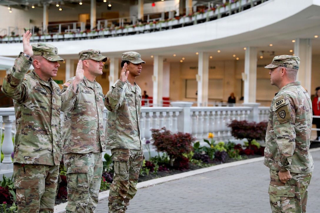 Three soldiers raise their right hands while facing another service member at a reception hall.