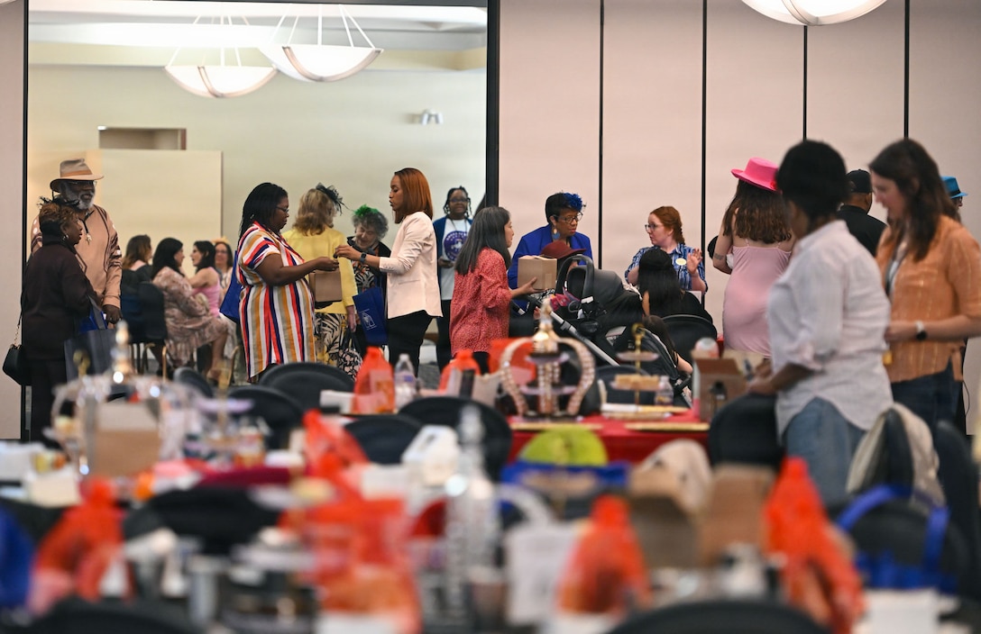 A group of military spouses stand in a large room chatting with tables in the foreground.