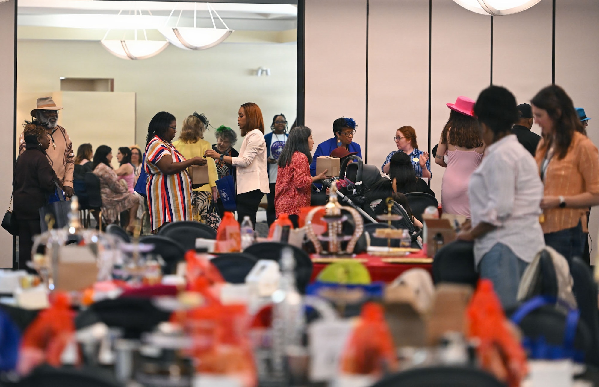A group of military spouses stand in a large room chatting with tables in the foreground.