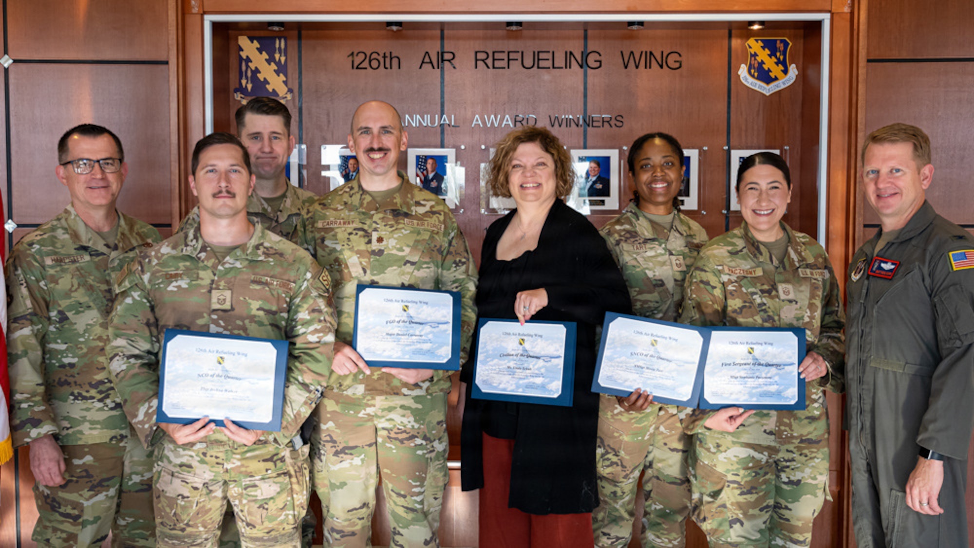 Airmen dress in camouflage and a civilian dress in black. All 6 holding certificates