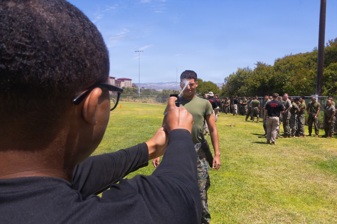 U.S. Marine Corps Staff Sgt. William Savory, left, a non-lethal weapons instructor with Expeditionary Operations Training Group, I Marine Expeditionary Force, sprays oleoresin capsicum into the eyes of  Pfc. Christian TeruelSerrano, a rifleman with 2nd Battalion, 5th Marine Regiment, 1st Marine Division, during a non-lethal weapons course at Marine Corps Base Camp Pendleton, California, April 28, 2026.