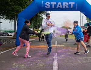 Two women spray colored powered on a man who is running.