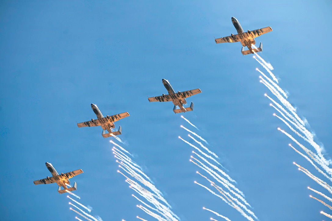 Four small planes fly in the air, with horizontal flares behind them.