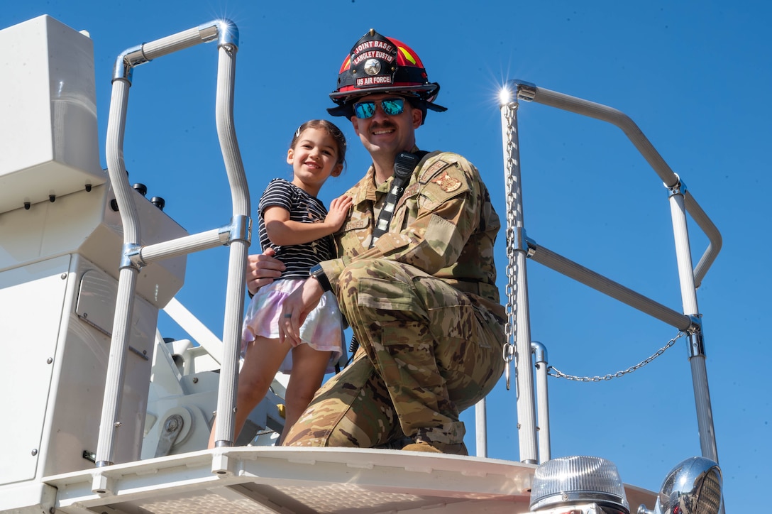 Photo shows a military firefighter on the right and his daughter on the left posing for a photo, smiling.