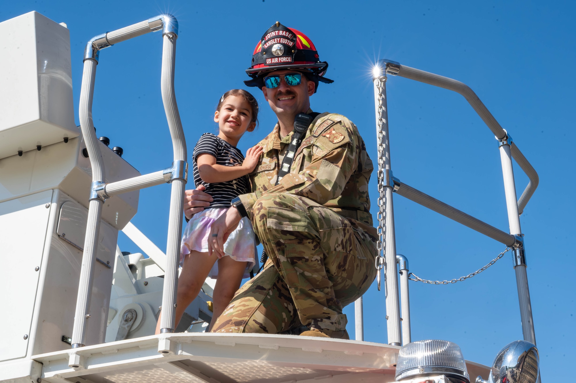Photo shows a military firefighter on the right and his daughter on the left posing for a photo, smiling.