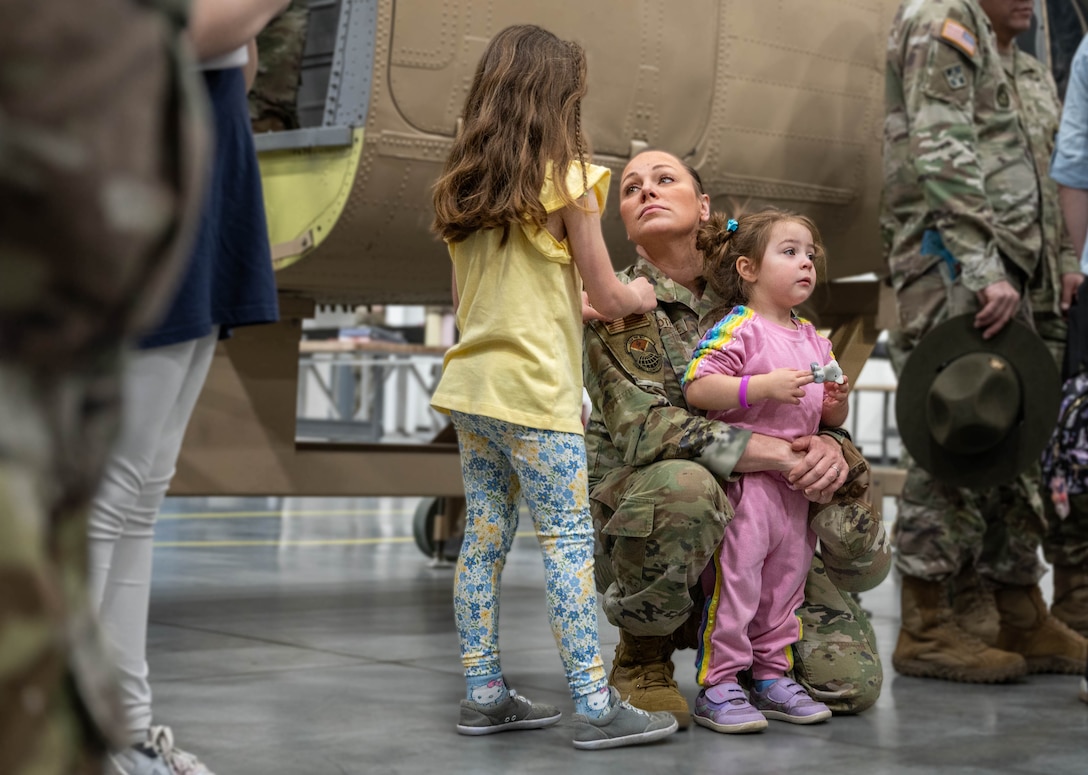 A military mom looks at her child on the left while holding another child in her arms.
