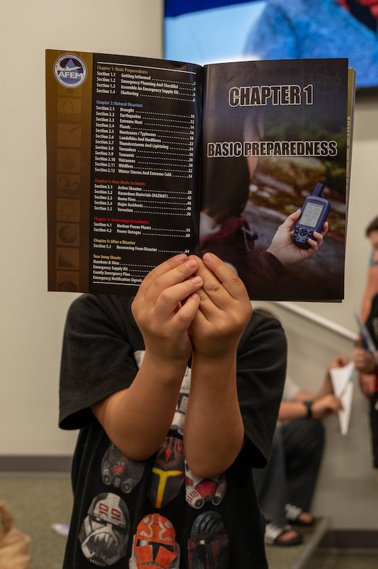 Photo shows a child holding a pamphlet in front of his face.