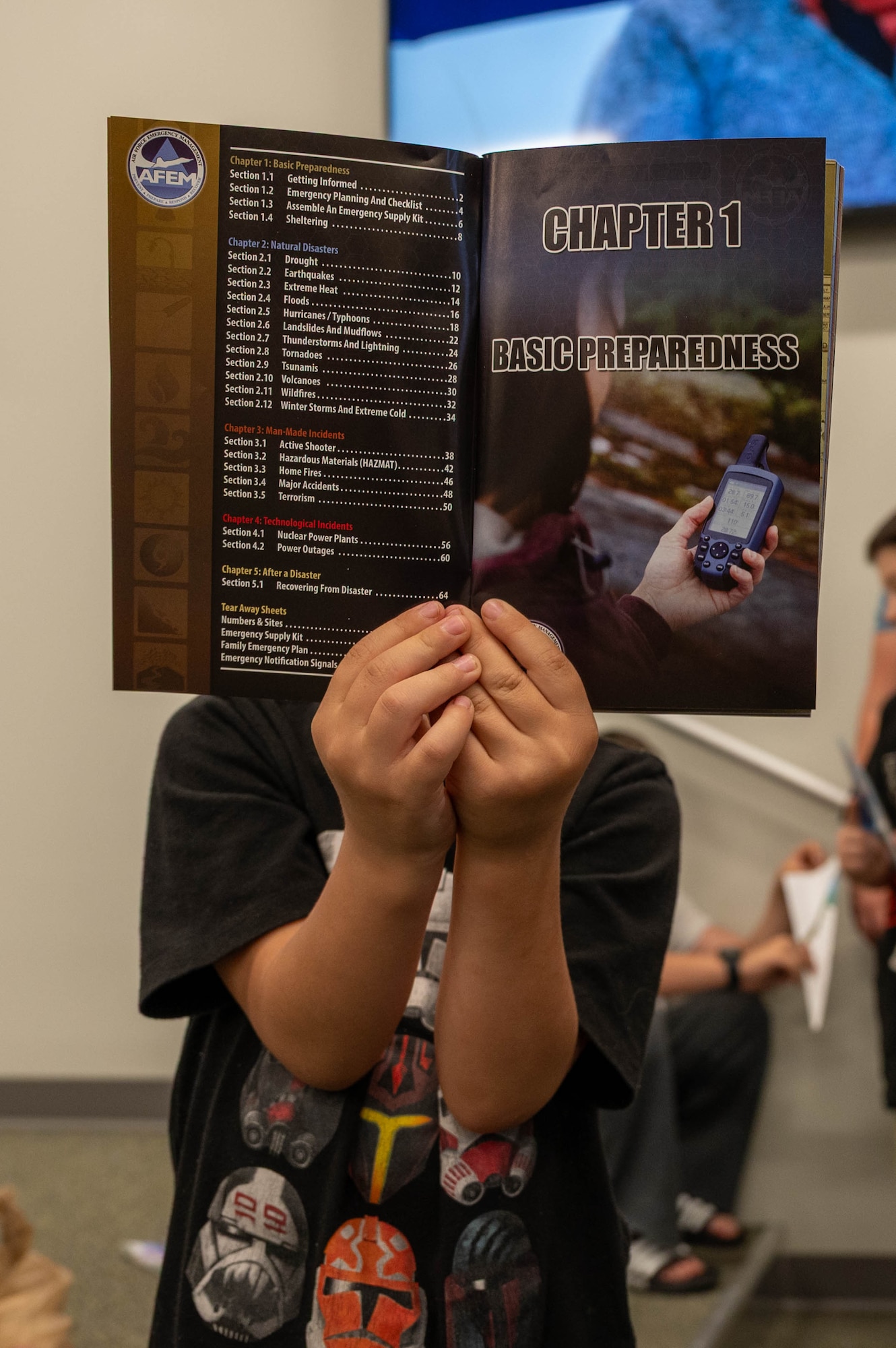 Photo shows a child holding a pamphlet in front of his face.
