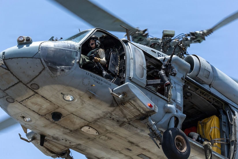 A helicopter lifts off in this close up image. The pilot is seated in the cockpit.