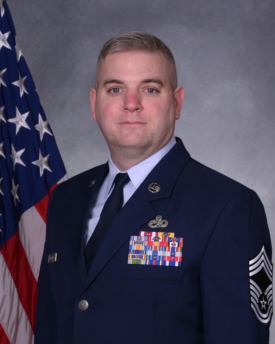 Man in uniform poses for photo in front of flag