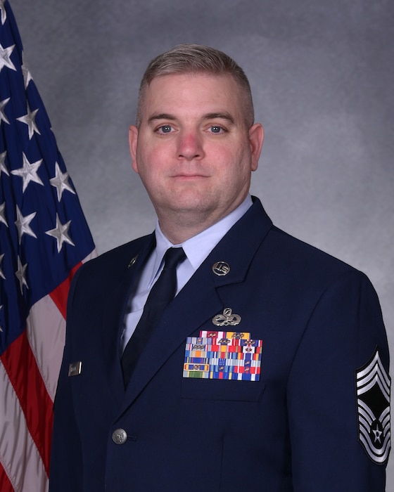 Man in uniform poses for photo in front of flag