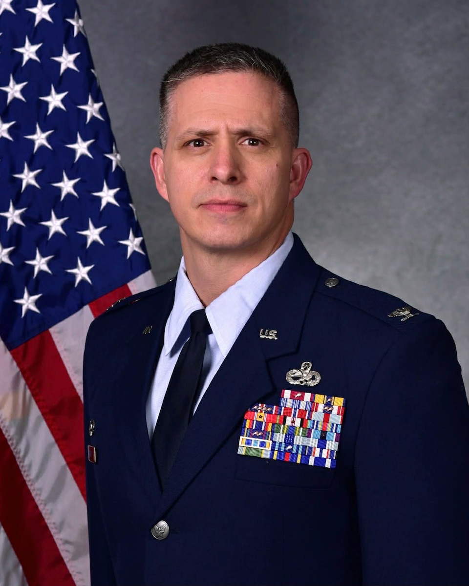 Man in uniform poses for photo in front of flag