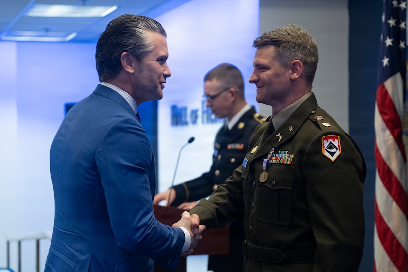 A side view of the secretary of war shaking hands with a service member.