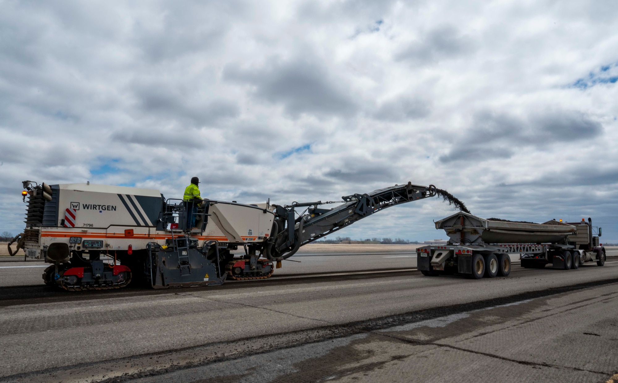 A truck pours asphalt into a dump truck.