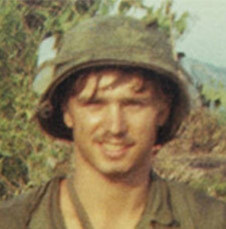 A man in a military uniform poses for a photo outdoors.