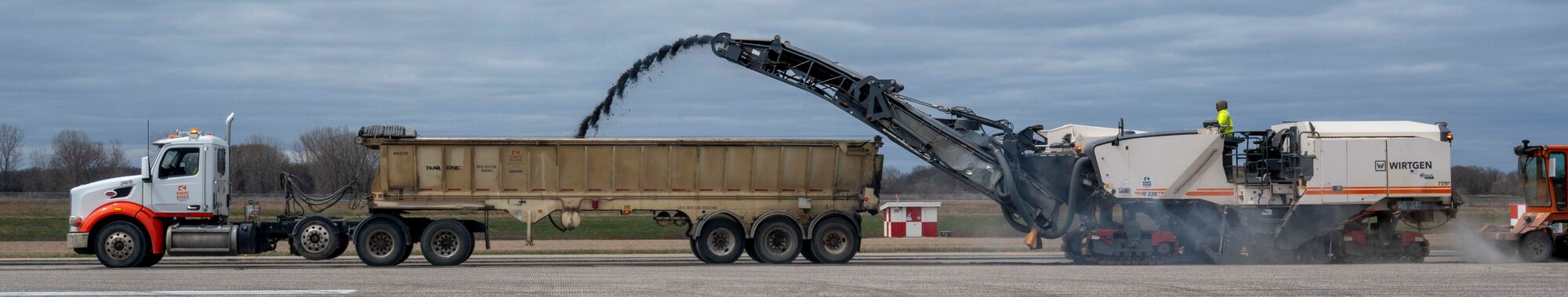 A truck pours asphalt into a dump truck.