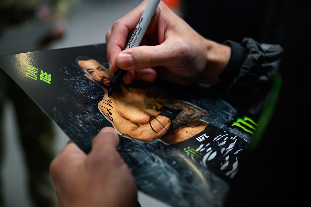 A person autographs a poster featuring a photo of himself.
