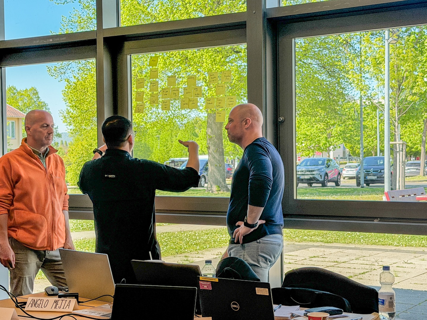 three people standing and talking in front of a window